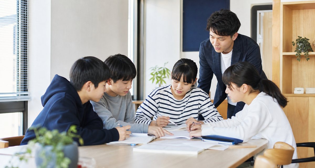 教室で、生徒が問題に取り組み、講師がそれを見ている様子